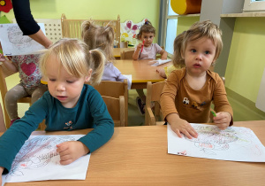 Alicja i Jasiu siedzą przy drewnianym stoliku i kolorują jeżyka.