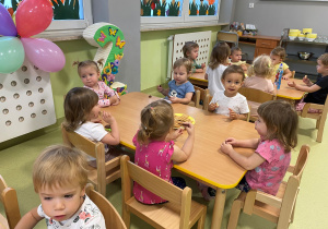 Dzieci siedzą przy stołach i jedzą urodzinowy poczęstunek.