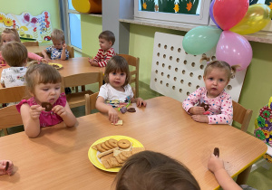 Dzieci siedzą przy drewnianym stole i częstują się urodzinowymi słodkościami.