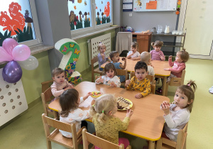 Dzieci siedzą przy stole i jedzą poczęstunek urodzinowy Apoloni
