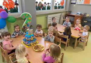 Dzieci siedzą przy stole i jedzą poczęstunek urodzinowy Jasia B.