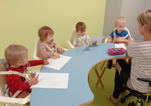 Dzieci siedzą przy stolikach i rysują kredkami.