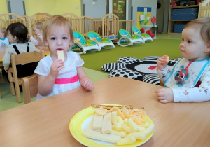 Lila z Marysią siedzą przy stoliku i częstują się urodzinowymi ciasteczkami.