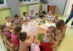 Dzieci siedzą przy stole i robią wspólną pracę plastyczną" Jesienne drzewo".