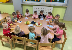 Dzieci siedzą przy stole oglądają i dotykają różne owoce.