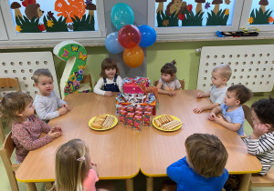 Dzieci siedzą przy stole i jedzą urodzinowy poczęstunek Zosi.