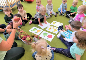 Dzieci siedzą na dywanie słuchając pogadanki o owocach.