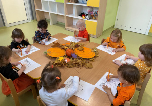 Dzieci siedzą przy stole i kolorują obrazek z dynią.