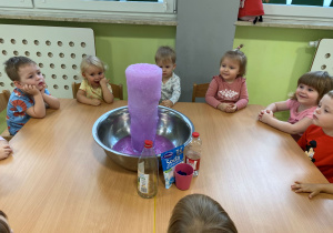 Dzieci siedzą przy stole i obserwują eksperyment wulkan.