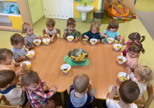 Dzieci siedzą przy stole i degustują zrobioną na zajęciach sałatkę.