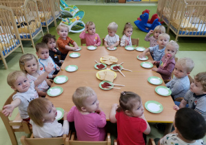 Dzieci siedzą przy stolikach przygotowanych do zajęć kulinarnych z waflami.