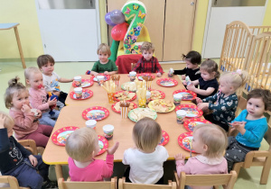 Dzieci siedzą przy wspólnym stole i częstują się smakołykami urodzinowymi.