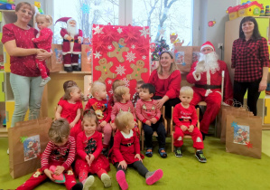 Dzieci z opiekunkami pozują do pamiątkowego zdjęcia z Mikołajem.