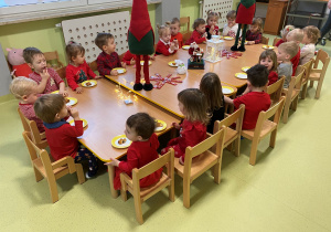 Dzieci siedzą przy drewnianym stole i zajadają słodki poczęstunek.