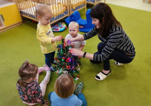 Dzieci z opiekunką ubierają choinkę.