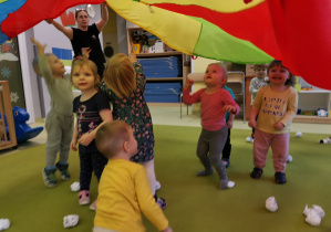 Dzieci bawią się wykorzystując chustę animacyjną i papierowe śniegowe kule.