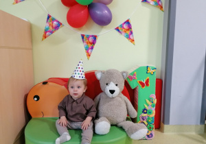 Oluś siedzi z misiem na dziecięcej kanapie przy urodzinowej jedynce.