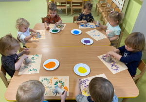Dzieci siedzą przy stole i wykonują prace plastyczną farbami.