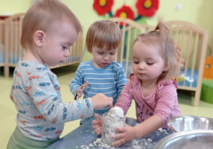 Wojtek, Nela i Janek wrzucają sztuczny śnieg do szklanki.