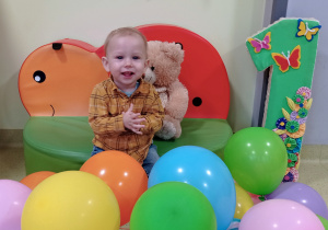 Józio siedzi na pufie wśród balonów.