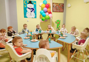 Grupa dzieci siedzi w fotelikach przy stole i świętuje urodziny Józia.