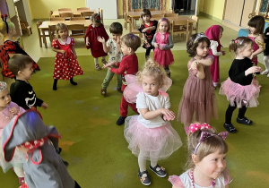 Dzieci w przebrane za różne postacie z bajek tańczą na dywanie.