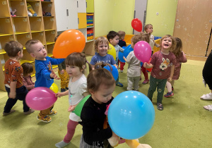 Dzieci tańczą na dywanie z kolorowymi balonami.