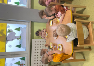 Dzieci siedzą przy stole i zajadają się pączkami z okazji " Tłustego czwartku".