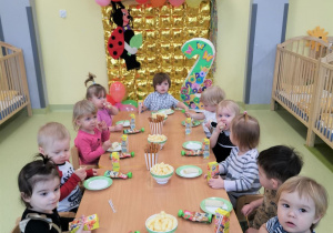 Dzieci siedzą przy stolikach przy urodzinowym poczęstunku.