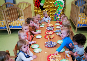 Dzieci siedzą przy stolikach podczas urodzinowego poczęstunku.