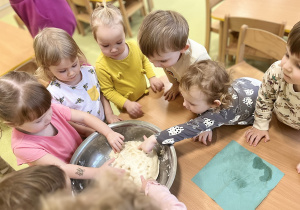 Dzieci stoją w około stołu i przygotowują na metalowej misce masę solną.