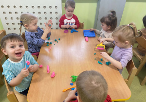 Dzieci siedzą przy stole i lepią figurki z masy plastycznej.