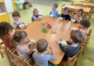 Dzieci siedzą przy stole i zajadają się deserem z kolorowych galaretek.