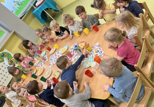 Dzieci siedzą przy drewnianym stoliku i zadają urodzinowe smakołyki