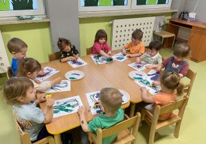 Dzieci siedzą przy stole i malują farbami kwiaty krokusy.