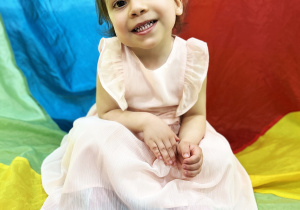 Julianka siedzi na kolorowej urodzinowej chuście.