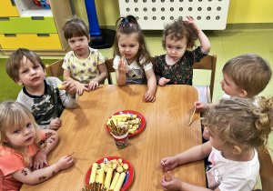 Dzieci siedż przy drewnianym stoliku na którym są położone smakołyki urodzinowe.