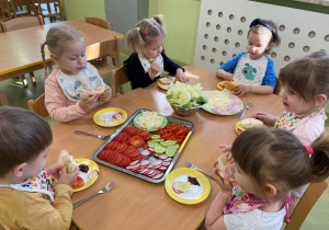 Dzieci siedzą przy stole i przygotowują samodzielnie wiosenne kanapki.