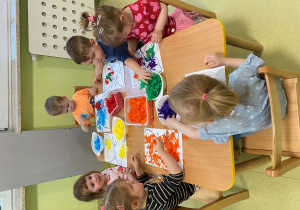 Dzieci siedzą przy stole i wyklejają kolorowe motyle z bibuły.