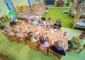 Dzieci siedzą przy stolikach w trakcie urodzinowego poczęstunku.