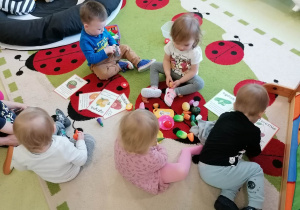 Dzieci siedzą na dywanie i zapoznają się z owocami i warzywami.