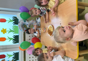 Dzieci siedzą przy stole i zajadają urodzinowy poczęstunek Maksymiliana.