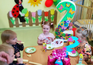 Marysia siedzi przy stoliku z dziećmi podczas urodzinowego poczęstunku.