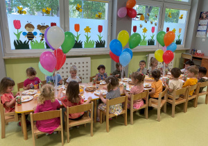 Dzieci siedzą przy stole podczas poczęstunku z okazji Dnia Dziecka.