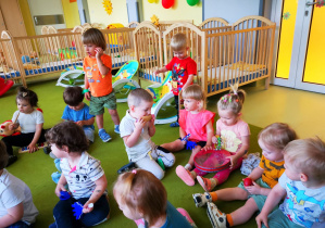 Dzieci siedzą na dywanie, grają na instrumentach muzycznych.
