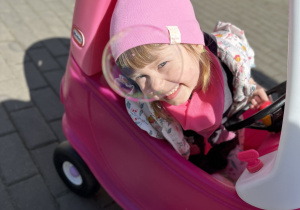 Blania siedzi w różowym samochodziku ogrodowym i spogląda na bańkę mydlaną.