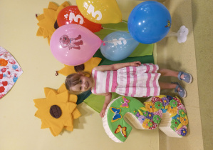 Weronika pozuje do urodzinowego zdjęcia przy cyferce trzy i kolorowych balonach.