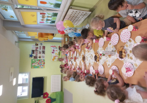 Dzieci siedzą przy stole i degustyją urodzinowy poczęstunek.
