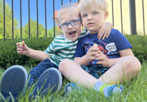 Szymon i Oskar siedzą na trawie i przytulają się.