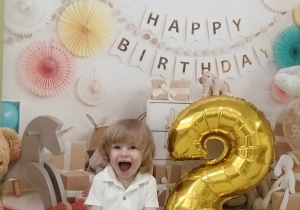 Jan pozuje do urodzinowego zdjęcia przy baloniku w kształcie cyfry 2.